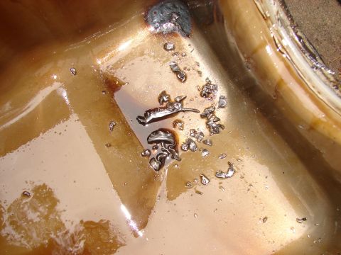 1973 Ford Ranchero - Close-up of metal fragments suspended in dark oil within a container.