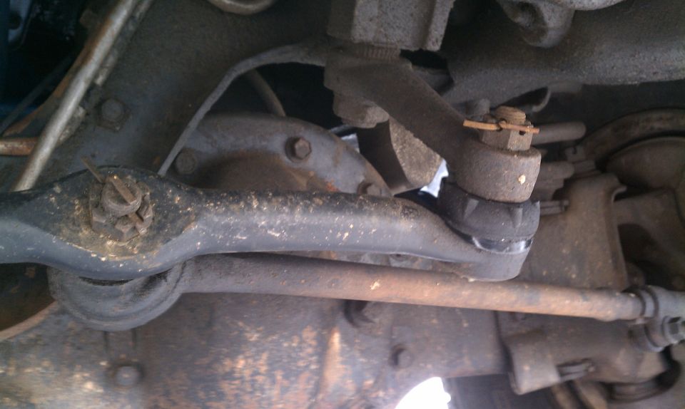 Underside view of tie rod end and steering linkage with rust and dirt on a 1984 Ford Bronco