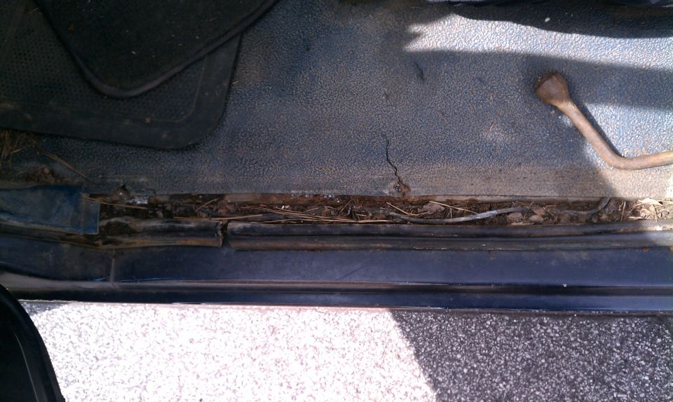 Interior floor of a vehicle with debris and rust along the door sill