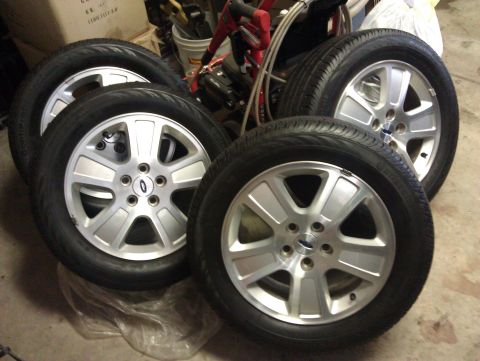 2007 Ford Crown Victoria - Four silver alloy wheels with tires are displayed, each bearing a Ford logo.