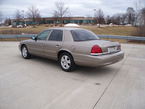 2007 Ford Crown Victoria - Tan 2007 Ford Crown Victoria parked on a concrete surface with a building in the background.