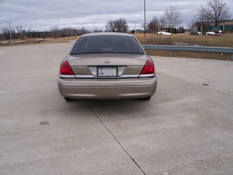 2007 Ford Crown Victoria - The rear of a tan sedan is shown parked on a concrete surface with a cloudy sky overhead.