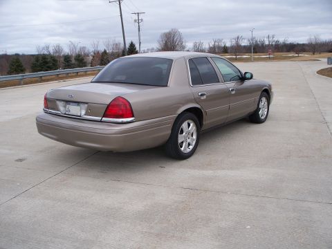 2007 Ford Crown Victoria - Rear 3/4 view of a tan 2007 Ford Crown Victoria sedan parked on concrete.