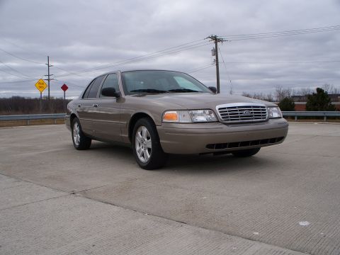 2007 Ford Crown Victoria - A tan 2007 Ford Crown Victoria sedan is viewed from the front three-quarter angle on a cloudy day.