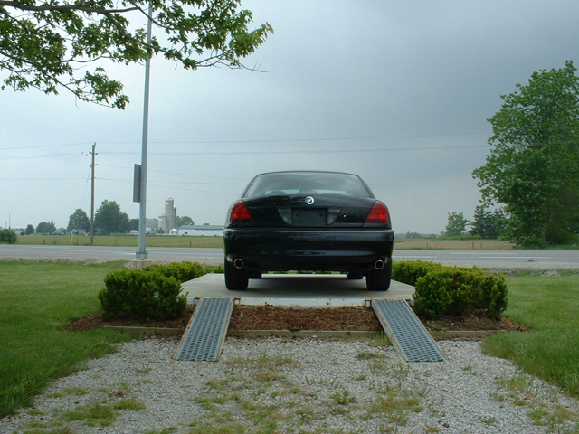 Black sedan parked on a concrete pad with ramps. Cloudy sky