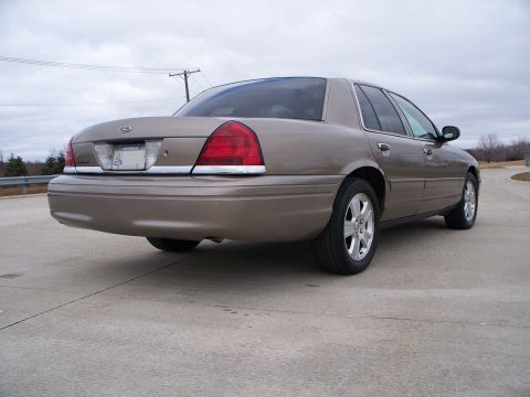 2007 Ford Crown Victoria - Rear three-quarter view of a tan 2007 Ford Crown Victoria sedan on a paved surface.