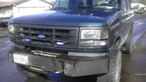1995 Ford Bronco - Front view of a 1995 Ford Bronco a dark green exterior, custom bumper, and blue lights integrated into the grille.