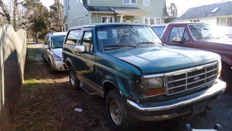 1996 Ford Bronco - A green Ford Bronco is parked in a driveway with other vehicles visible.