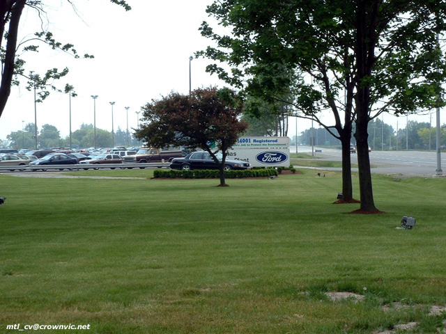 Ford plant entrance sign with blue Ford oval in a grass median beside a parking lot