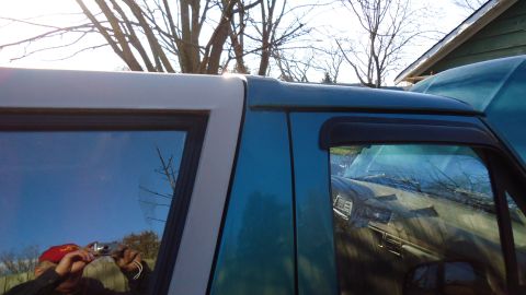 1996 Ford Bronco - The side profile of a 1996 Ford Bronco is visible, with another vehicle reflected in the window.