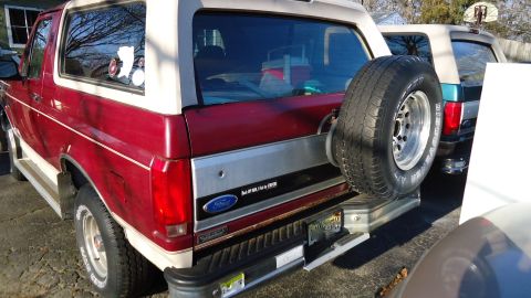 1996 Ford Bronco - Rear view of a red and white Ford Bronco with a spare tire, parked outdoors next to another vehicle.