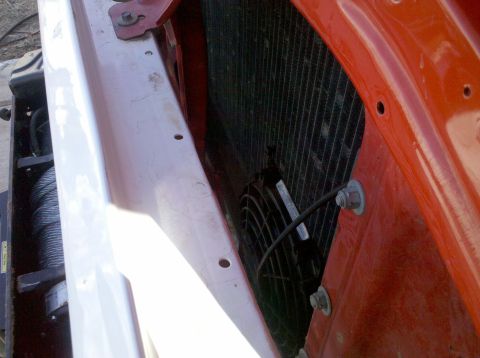 1979 Ford Bronco - A close-up view of the front of a vehicle shows a radiator with an electric fan mounted to it. The surrounding body panels are painted brig…