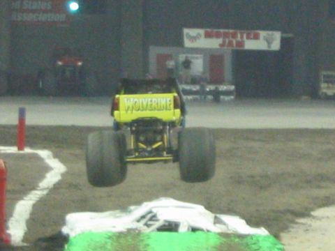 1986 Ford Bronco - A monster truck jumps over a wrecked car during an event.
