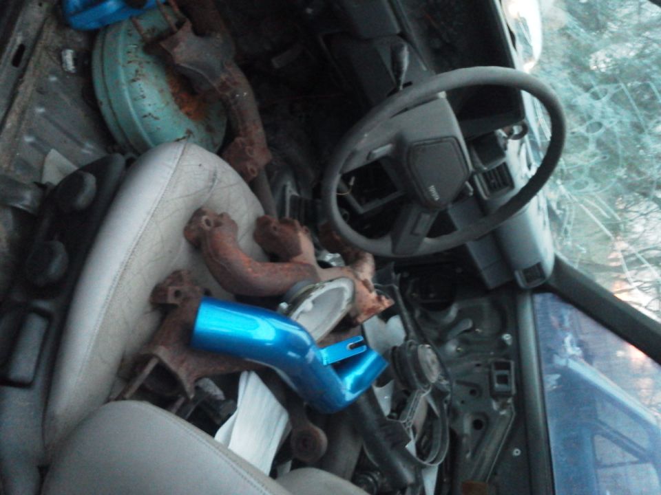 Interior of a vehicle with seats, steering wheel, and various engine parts piled up