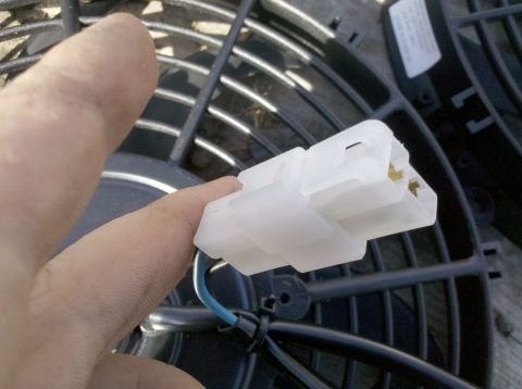 1979 Ford Bronco - A hand holds a white electrical connector with a blue wire, positioned in front of a cooling fan's grille.