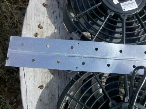 1979 Ford Bronco - A metal bracket is positioned over two electric fans, resting on a weathered wooden surface.