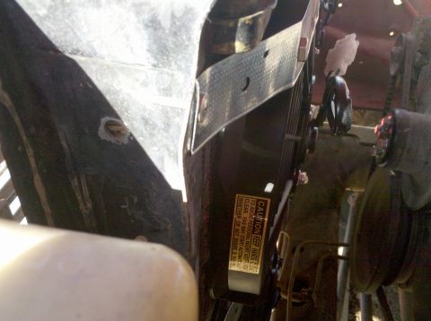 1979 Ford Bronco - A close-up view of engine components, including a fan and belts, with a caution sticker visible.