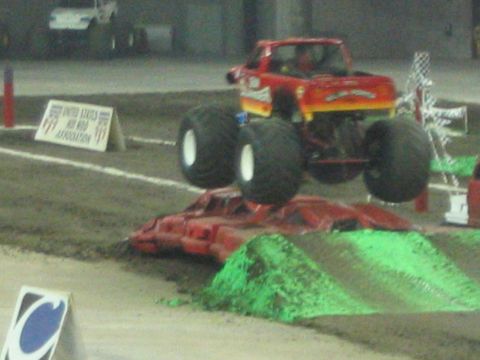 1986 Ford Bronco - A monster truck soars through the air during an event, with another vehicle visible in the distance.