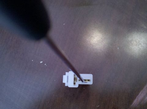 1979 Ford Bronco - A screwdriver is used to manipulate the contacts within a white electrical connector.