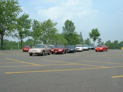 2000 Ford Crown Victoria - Several cars are parked in an asphalt lot under a partly cloudy sky.