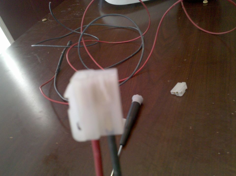 Close-up of white electrical connectors and red and black wires on a wooden surface. A small tool is also visible