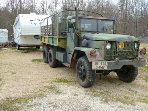 1992 Ford Mustang - A military truck with a trailer hitched to its rear is parked on a gravel lot.