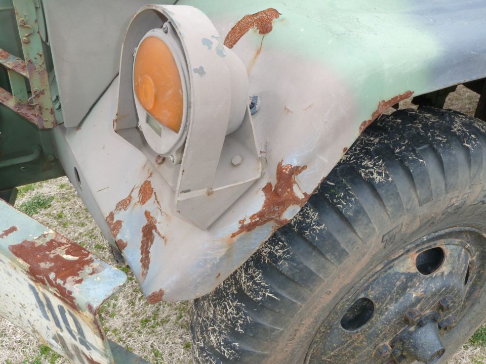 Close-up of a rusty truck fender with an orange headlight and large tire
