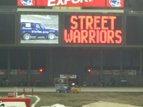1986 Ford Bronco - A blue SUV is shown on a stadium screen with the text "STATION.AUTO" visible on its side.