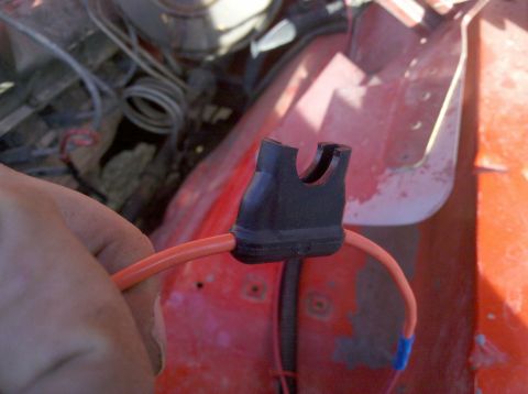 1979 Ford Bronco - Close-up of a hand holding an orange wire with a black connector, part of engine bay wiring.