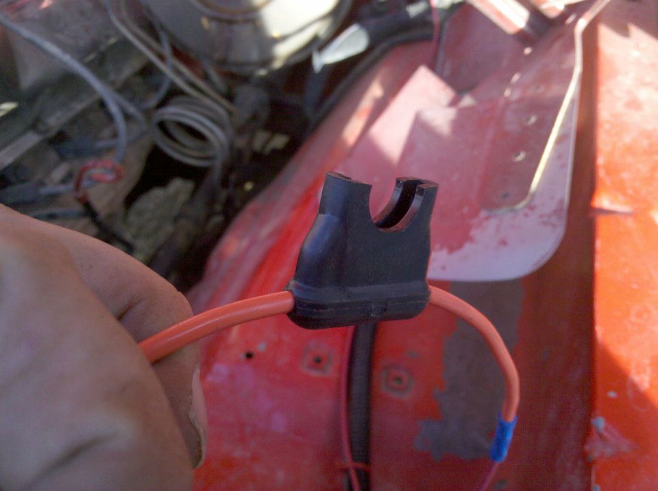 Hand holding orange wire with black connector attached to red body panel