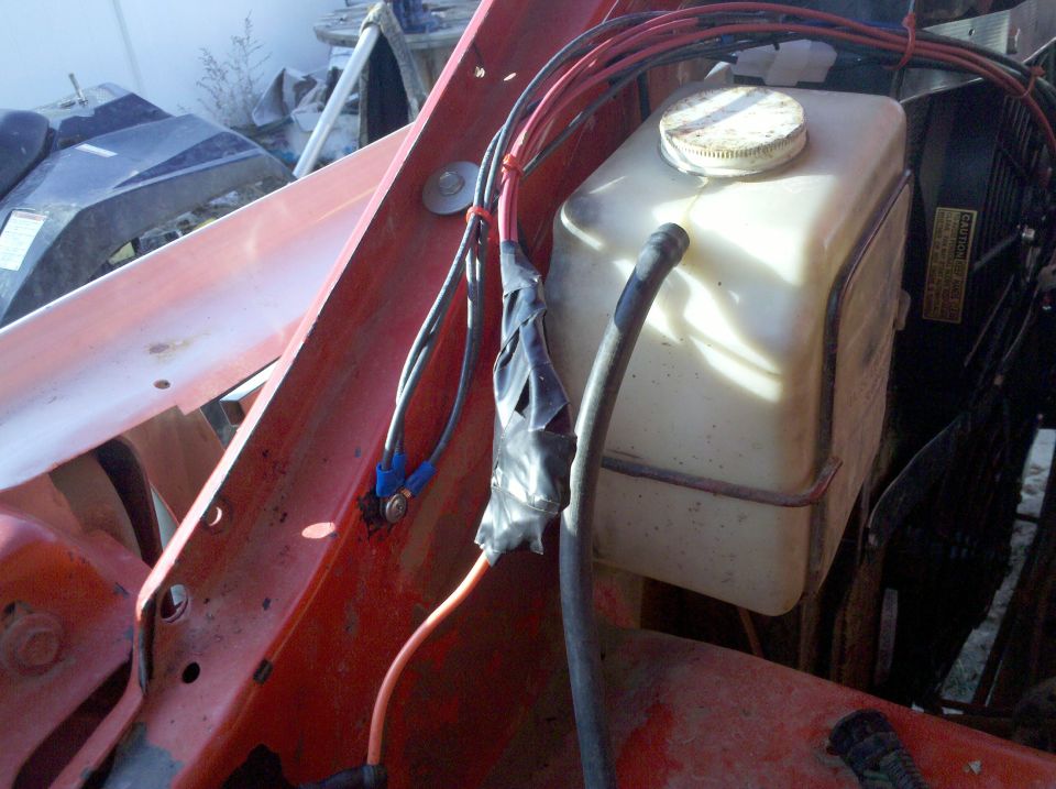 Engine bay wiring and fluid reservoir with "CAUTION" label visible