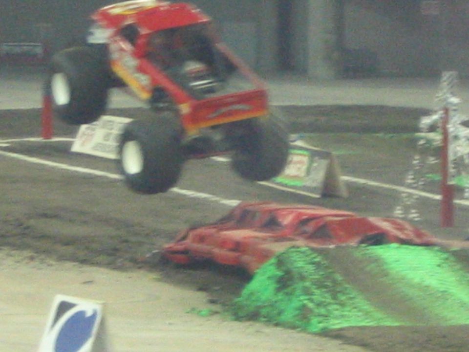 Red monster truck mid-air over a dirt ramp