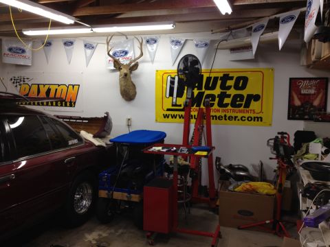 1992 Ford Crown Victoria - A red 1992 Ford Crown Victoria is parked inside a garage with various racing memorabilia on the walls.