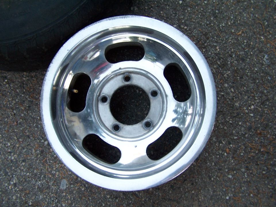 Aluminum alloy wheel with five lug holes and oval cutouts, resting on asphalt