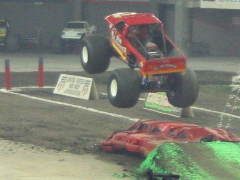 1986 Ford Bronco - A monster truck soars through the air during an event, with another vehicle visible in the background.