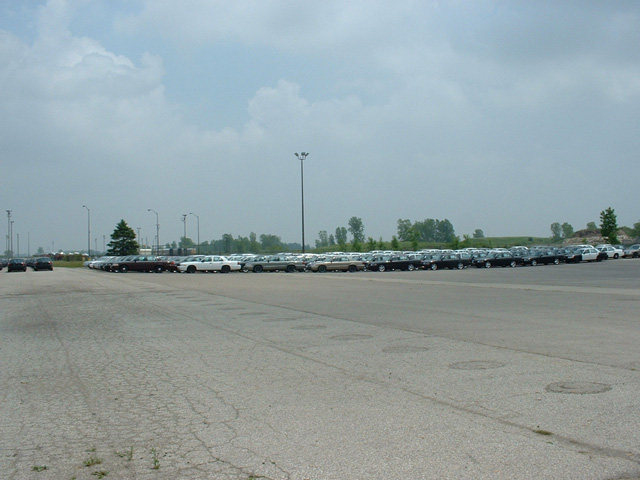 Long line of parked cars across a large cracked asphalt lot under a hazy sky