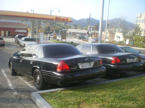 2004 Ford Crown Victoria - Two black Ford Crown Victorias are parked at a Shell gas station, with mountains in the background.