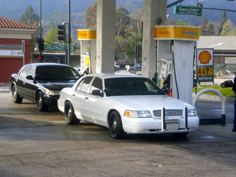 2004 Ford Crown Victoria - Two Ford Crown Victoria police cars are seen at a Shell gas station, one white and one black.