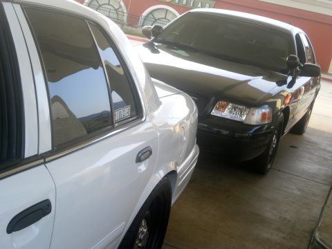 2004 Ford Crown Victoria - Two Ford Crown Victoria police interceptors parked side-by-side. One is white, the other is black.