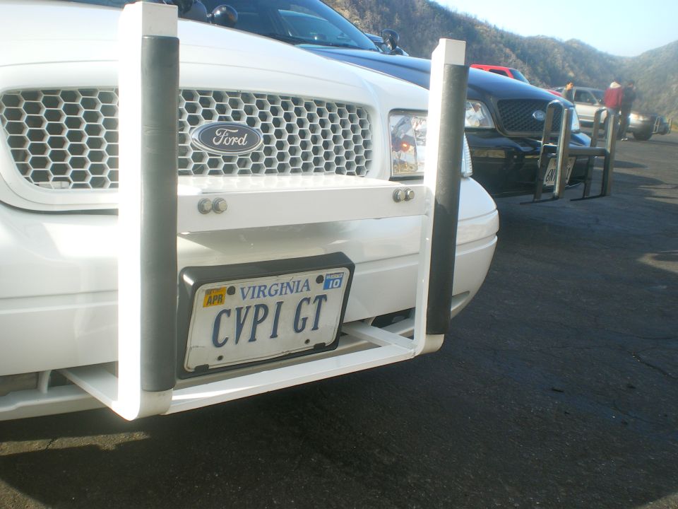 Front of a white Ford Crown Victoria with a push bar and Virginia plates. Another black Crown Victoria is behind it
