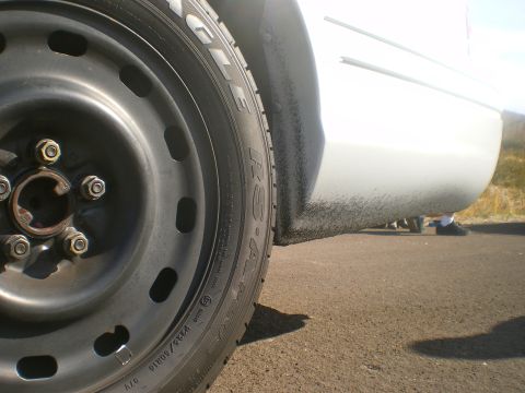 2004 Ford Crown Victoria - A close-up view of a car's steel wheel and lower side panel, showing tire details and road grime.