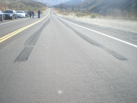 2004 Ford Crown Victoria - Tire marks are visible on the asphalt road, with multiple vehicles parked on the side.
