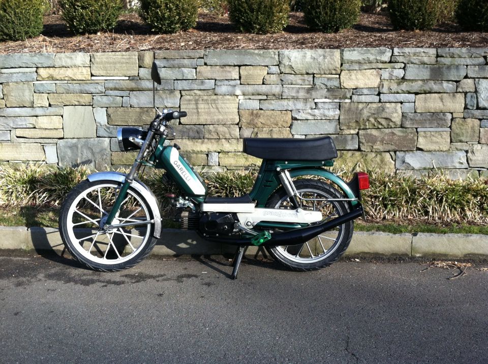 Green moped with white fenders and white-spoked wheels parked on asphalt