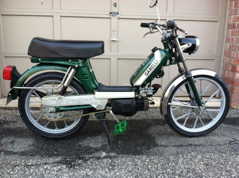 1981 Garelli Rally Sport - A green moped with chrome accents and pedals is parked in front of a garage door.