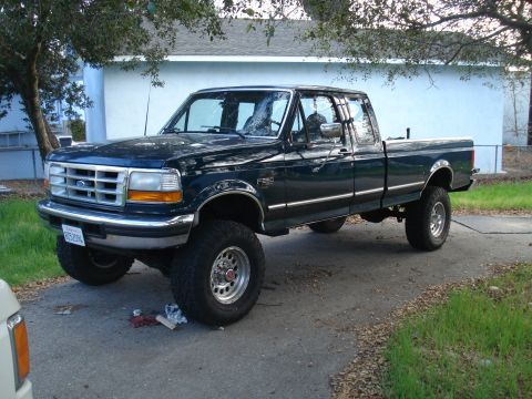 1994 Ford F-250 - A dark green Ford F-250 pickup truck is parked on a paved surface in front of a house.