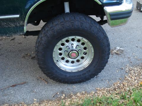 1994 Ford F-250 - Close-up of a truck's wheel and fender shows off-road tire and chrome rim.