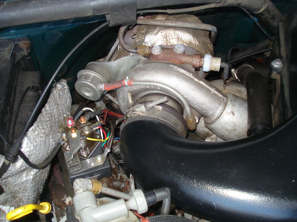 Close-up of a turbocharger, exhaust manifold, and wiring harness in an engine bay