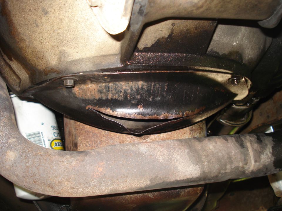 Underside of a vehicle showing an oil filter, exhaust pipe, and a bent metal shield