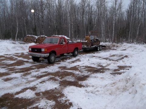 1987 Ford F-250 - A red 1987 Ford F-250 pickup truck is seen towing a bulldozer on a trailer in a snowy, wooded environment.