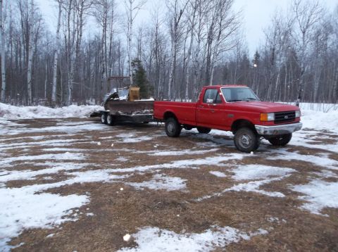 1987 Ford F-250 - A red 1987 Ford F-250 pickup truck is seen from a 3/4 front angle, towing a trailer with a plow in a snowy, wooded area.